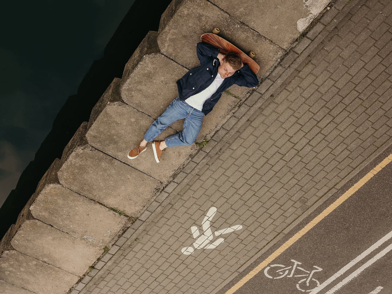 About Young man in denim lounging on sidewalk with skateboard, enjoying leisure outdoors.